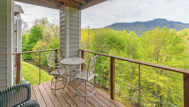 A wooden deck with a table and chairs, overlooking a lush green landscape with mountains in the distance. - Hawks Peak South 221-Mtn Condo, Near High Country Attractions, ZipLining, Hiking (Seven Devils)