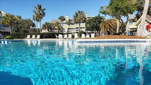 Una piscina azul cristalina con sillones de descanso y palmeras al fondo.