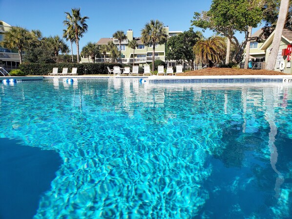 A clear blue pool with lounge chairs and palm trees in the background.