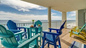 A balcony with blue Adirondack chairs, a small table with a vase and pastries, and a view of the ocean.