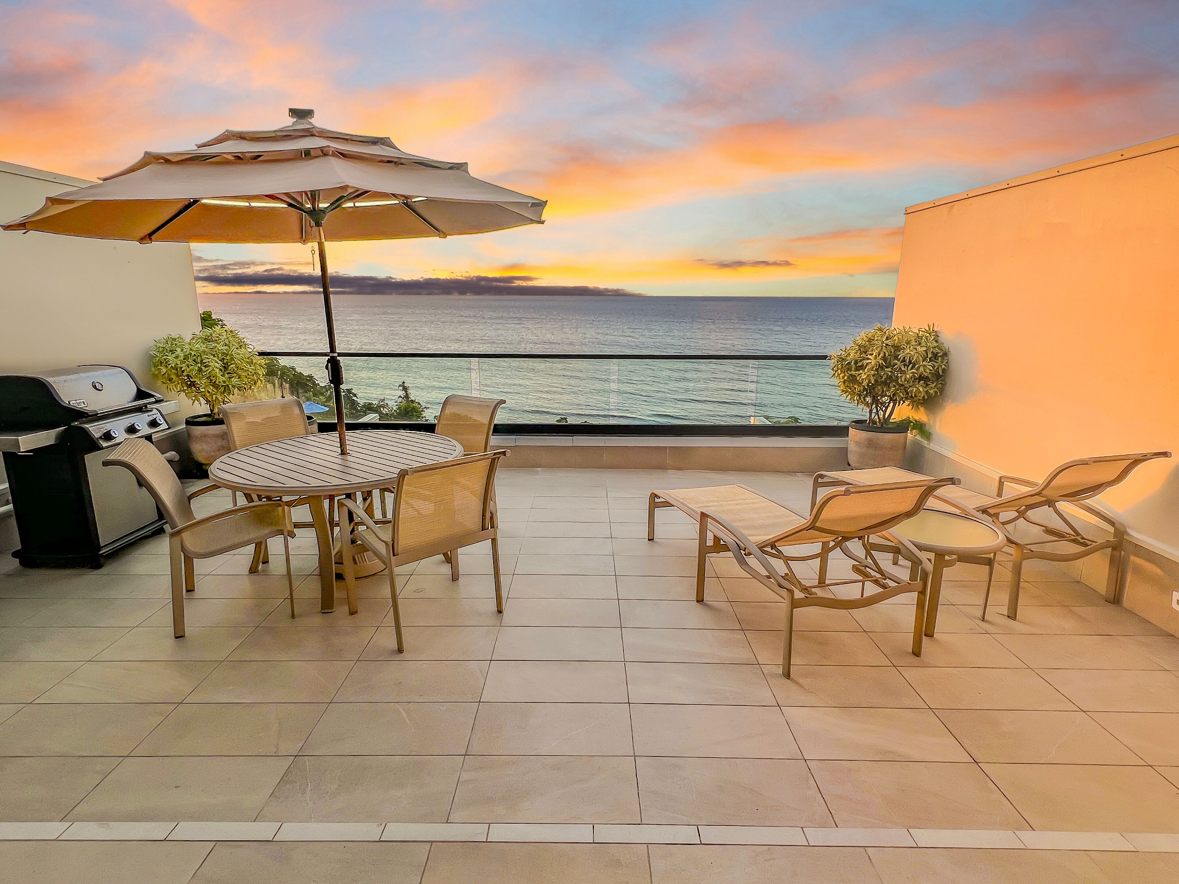A patio with a round table and chairs, a grill, and a view of the sea.