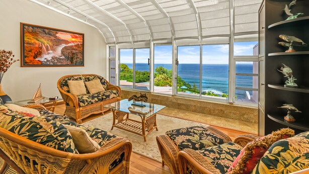 A spacious room with wicker furniture, a glass coffee table, and a large painting of a waterfall. - WORLD CLASS#402 Superior PENTHOUSE, Full AC, 2 Suites, Best Views & Privacy (Princeville)