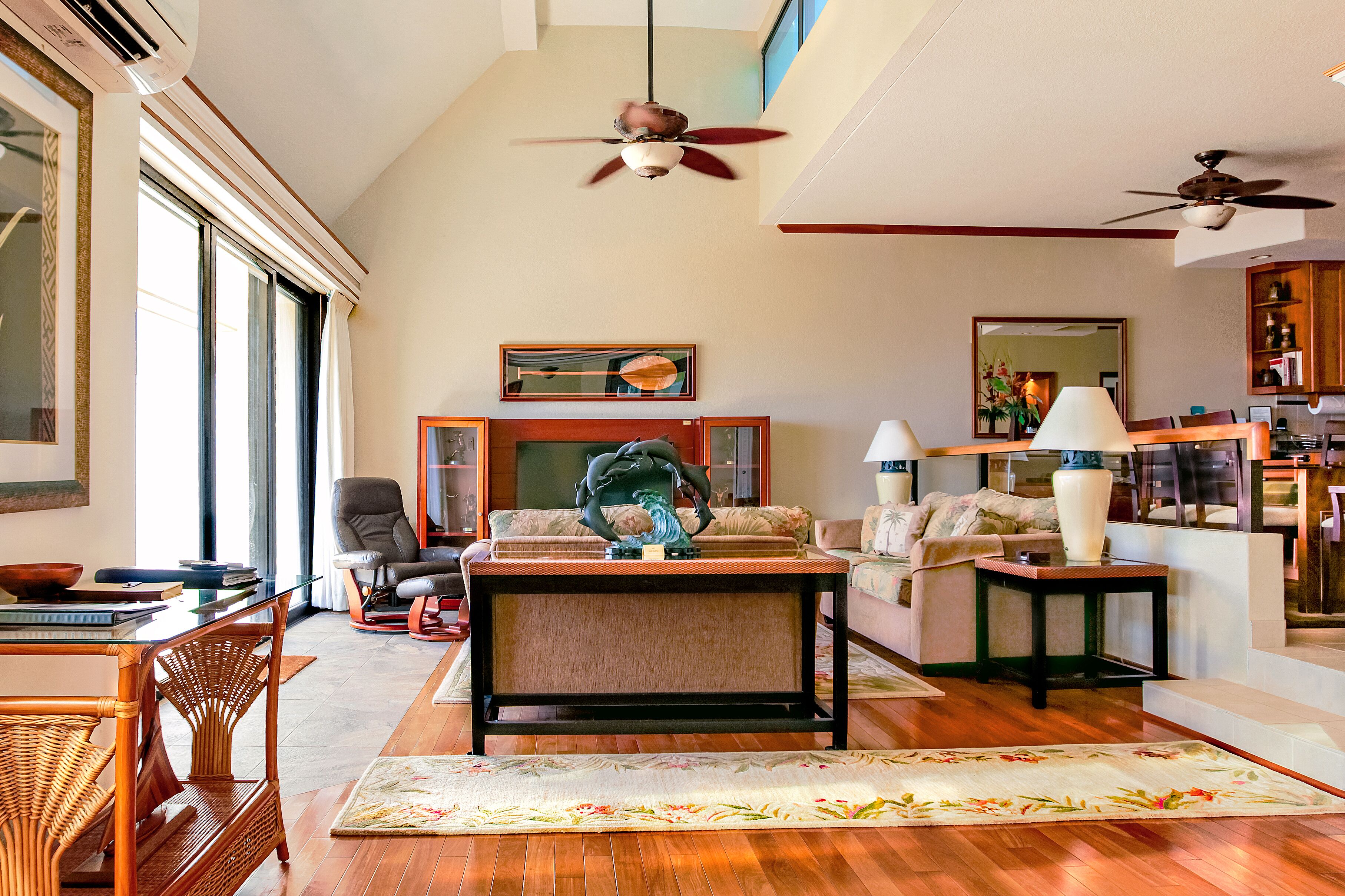 A spacious living room with a large window, ceiling fans, a sofa, a coffee table, and a bookshelf.