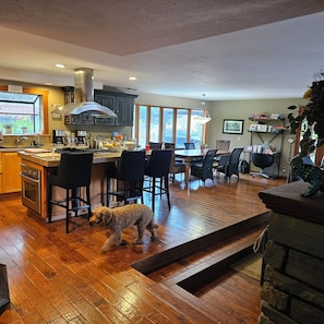 A kitchen with wooden flooring, a dining area with chairs, and a dog walking through.
