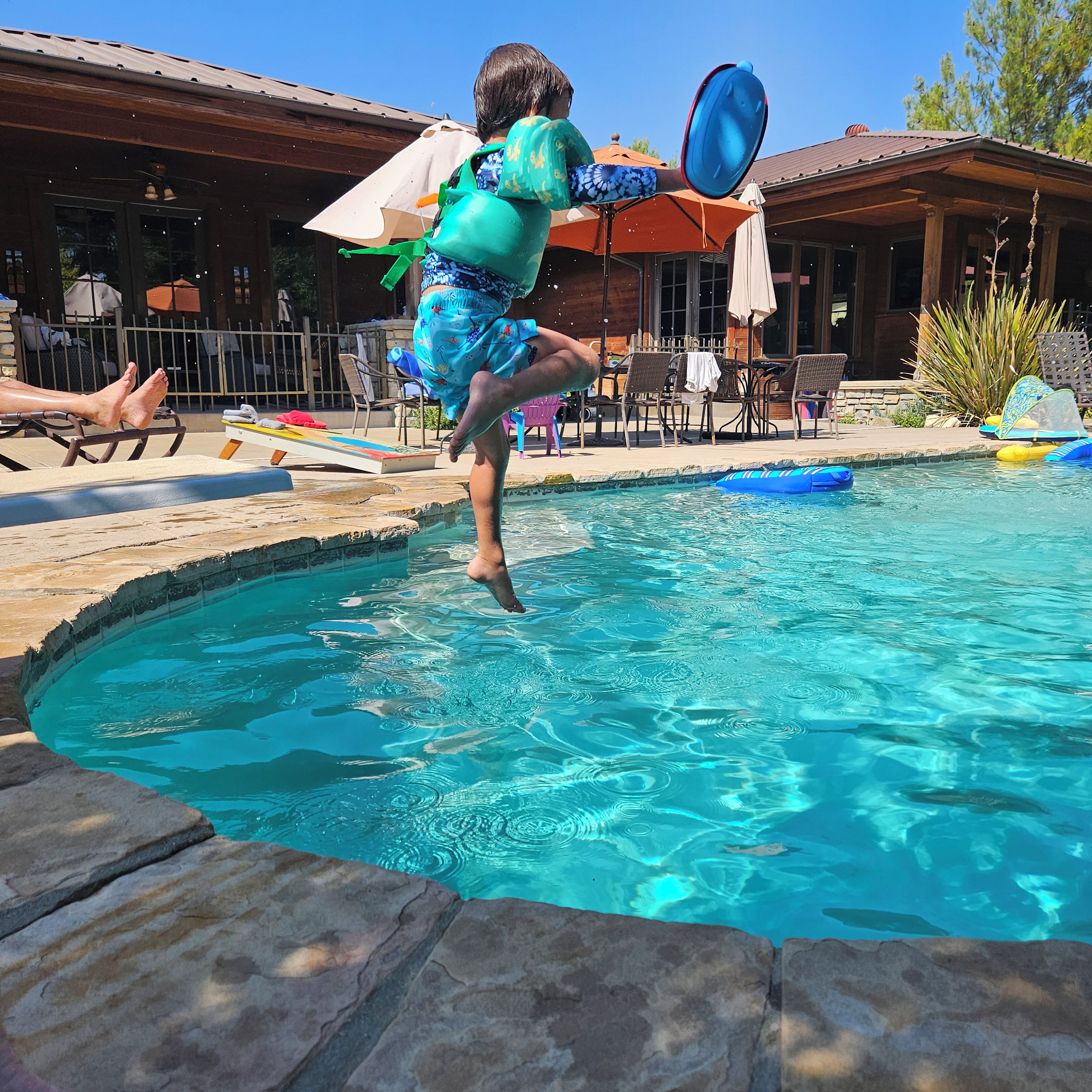 A person jumping into a pool with a blue inflatable ring.