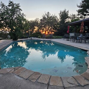 Piscina com borda de pedra, cercada por árvores e área de terraço com mobiliário de exterior.