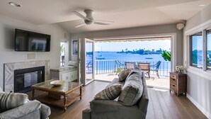 A spacious living room with a fireplace, a flat-screen TV, a ceiling fan, and a large sliding glass door leading to a balcony with a view of the ocean. - Right On The Beach! Exquisitely Remodeled 3BR/3BA . Perfect For Families. (San Diego)