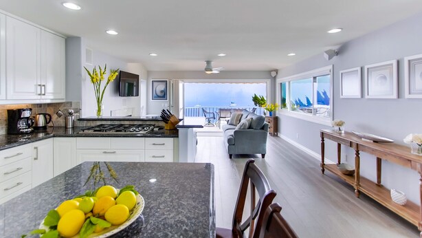 A modern kitchen with white cabinets, a granite countertop, and a dining area with a table and chairs. - Right On The Beach! Exquisitely Remodeled 3BR/3BA . Perfect For Families. (San Diego)