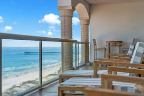 A balcony with wooden chairs and a view of the ocean and pier.