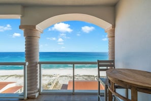 A balcony with a view of the ocean, a wooden table, and a chair.