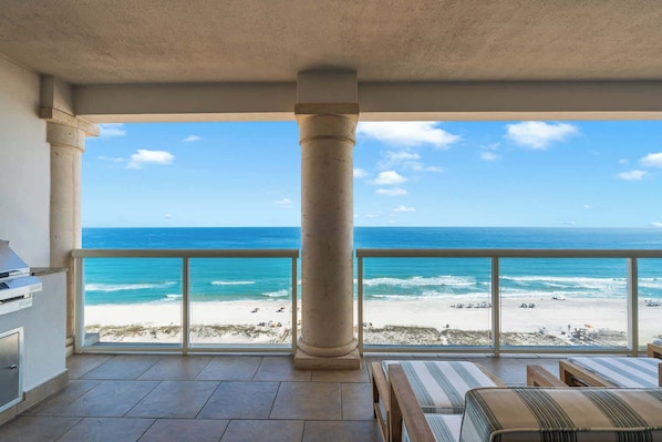 A balcony with a view of the ocean, a grill, and seating area.