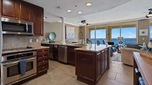 A modern kitchen with stainless steel appliances, a large island, and a view of the ocean. - Beach Club 1005 - 𝑨𝒒𝒖𝒂 𝑶𝒂𝒔𝒊𝒔 (Pensacola Beach)