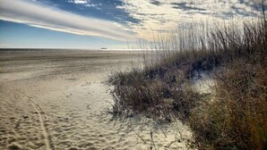Una platja amb sorra, vegetació escassa i un vaixell al capdamunt.