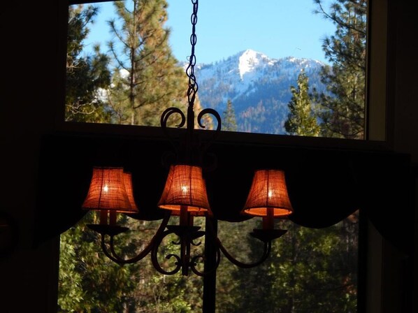 Un candelabro con tres lámparas frente a una ventana con vistas a la montaña.