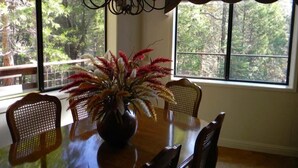 Un comedor con una mesa de madera, sillas, un florero con plantas secas y una araña.