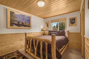 Une chambre à coucher dans une cabane en bois, avec un lit, une fenêtre, une lampe et un tableau représentant un paysage de montagne.