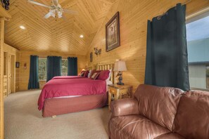 A wooden cabin bedroom with a bed, a leather couch, a ceiling fan, and a window with curtains. - Moose Inn - 22 Miles to YNP ~ Wifi ~ BBQ ~ Firepit (Island Park)