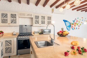 A modern kitchen with a gas stove, microwave, and sink. There are decorative wall stickers and a bowl of fruit on the counter.