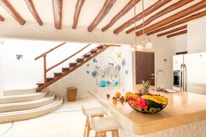 A kitchen with a central island, a wooden staircase, and a hanging light fixture.