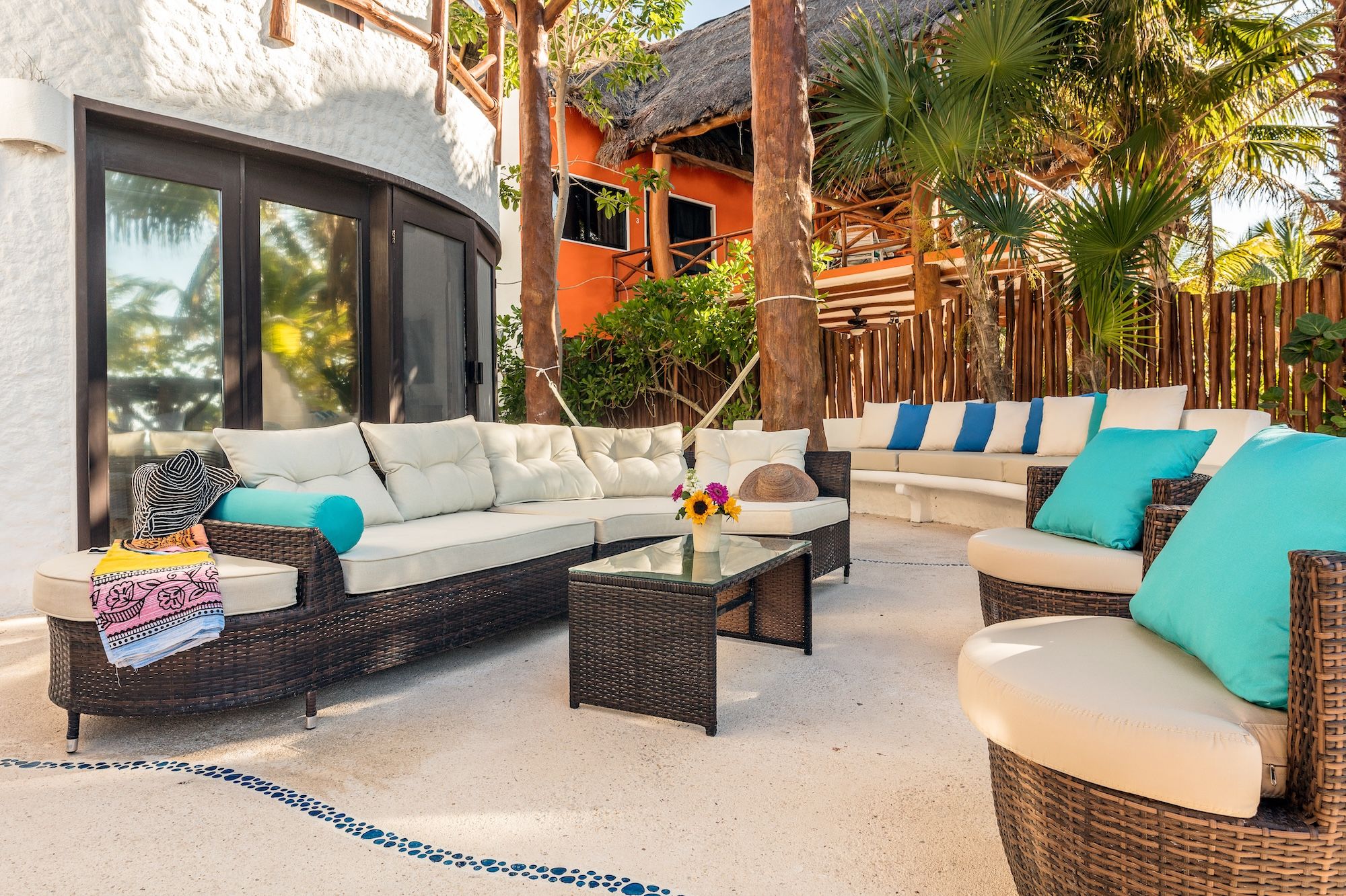 An outdoor seating area with wicker furniture and cushions, a glass coffee table, and a decorative vase with flowers.
