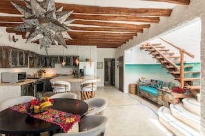 A spacious kitchen with a central island, wooden ceiling beams, and a rustic staircase leading to a balcony.