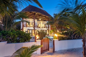 A beachfront property with a thatched-roof structure, a pool, and lush tropical vegetation.