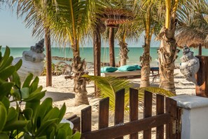 A beach setting with a wooden pergola, palm trees, and a bench with cushions.
