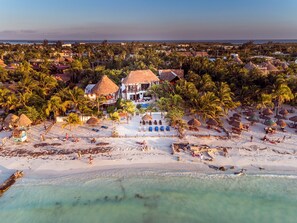 A beachfront property with a central building surrounded by palm trees and beach huts.