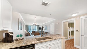 A modern kitchen with granite countertops, white cabinetry, and a built-in dishwasher. - Waterscape A317 ~ 2BR + Bunkroom  ~ Beach Service! (Fort Walton Beach)