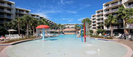A hotel pool area with multiple levels of balconies, palm trees, and lounge chairs.
