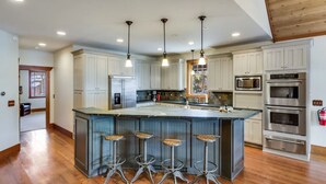 Une cuisine spacieuse dotée d’un grand îlot central, d’appareils électroménagers en acier inoxydable et de luminaires suspendus.