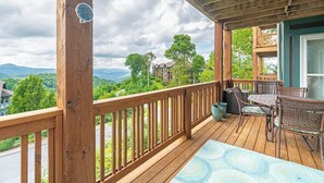 Une terrasse en bois avec une table et des chaises, offrant une vue panoramique sur un paysage pittoresque, avec des arbres et des montagnes.
