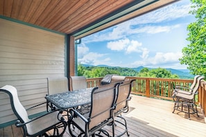 Um deck coberto ao ar livre com mesa e cadeiras, com vista para uma paisagem montanhosa.