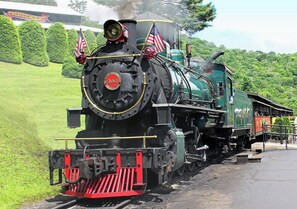 A steam locomotive with American flags, a 'TWEETSIE MINING' sign, and a lush green landscape in the background. - Townhome R5B- Mtn Home/View, Foosball, Indoor/Outdoor Pools & Hot Tub, Fireplace (Banner Elk)
