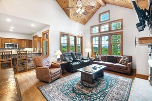 A spacious living room with a large window, a fireplace, and a high ceiling with wooden beams. - Townhome R5B- Mtn Home/View, Foosball, Indoor/Outdoor Pools & Hot Tub, Fireplace (Banner Elk)