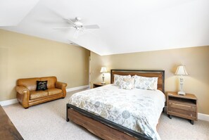 A bedroom with a bed, a nightstand, a lamp, a ceiling fan, and a leather couch. - Townhome R5B- Mtn Home/View, Foosball, Indoor/Outdoor Pools & Hot Tub, Fireplace (Banner Elk)