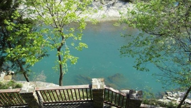 Un escalier en pierre mène à un lac d’un bleu limpide, bordé d’arbres.