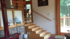 Un vaste espace de vie agrémenté d’un escalier en bois, d’un poêle à bois rouge, d’une table basse en verre et d’un tapis aux couleurs vives.