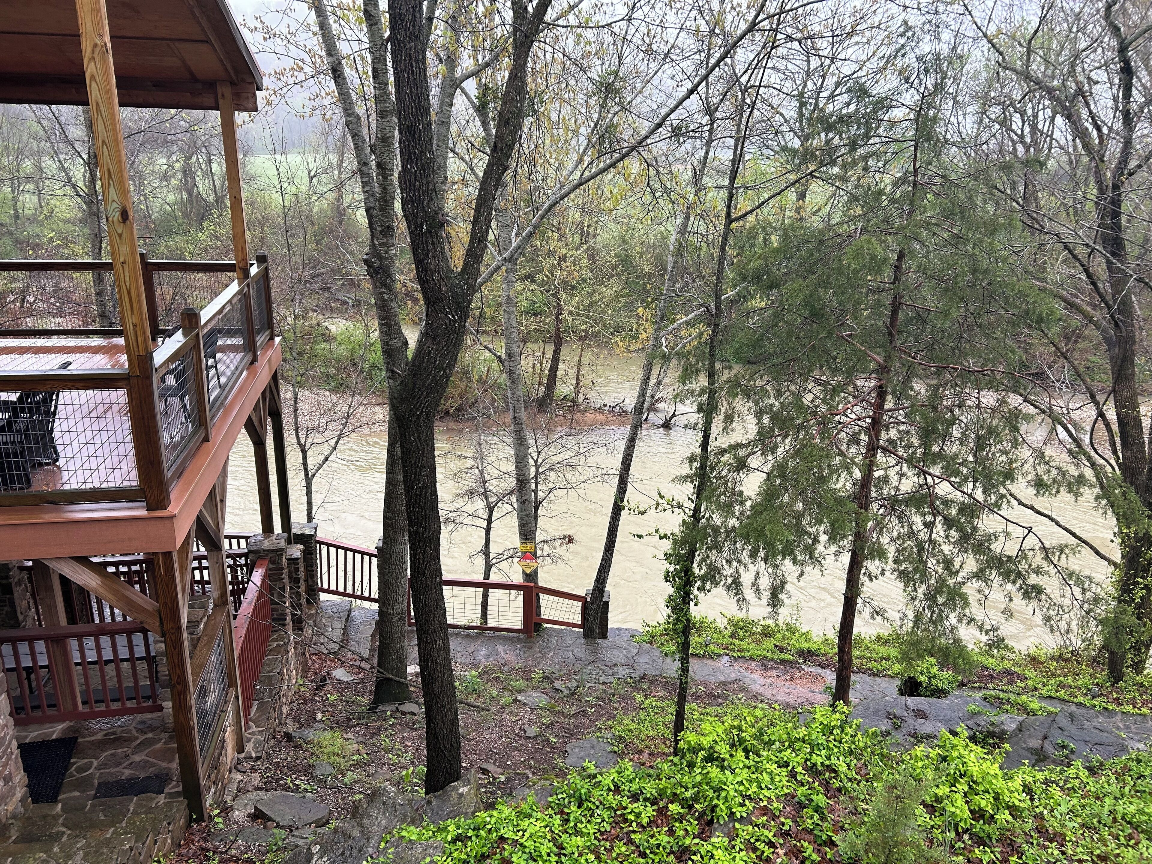 A wooden deck overlooking a river with trees and a stone wall.