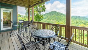 A wooden deck with a round table and chairs, overlooking a lush green landscape. - Wintergreens R1012- Mtn Condo/View, Gated Resort, Indoor/Outdoor Pools & Hot Tub (Boone)
