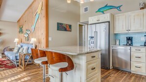 Una cocina con una isla de madera, taburetes de bar, un refrigerador y una cafetera.