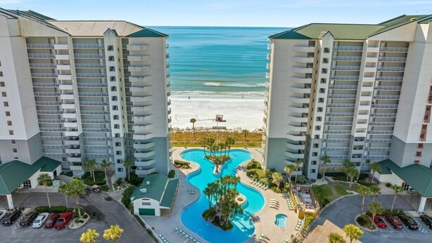 Ein Hochhaus-Hotel mit einem zentral gelegenen Schwimmbad, Blick auf den Strand und mehreren Parkplätzen.