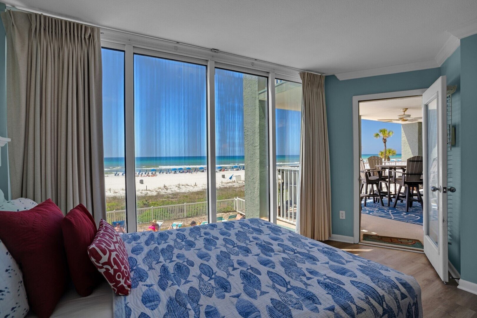 A bedroom with a large bed, a view of the beach, and a balcony with outdoor seating.