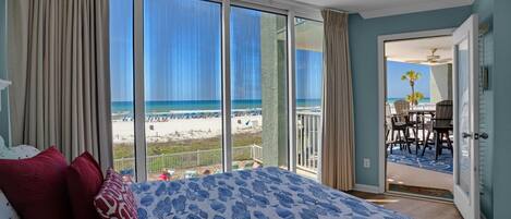 A bedroom with a large bed, a view of the beach, and a balcony with outdoor seating.