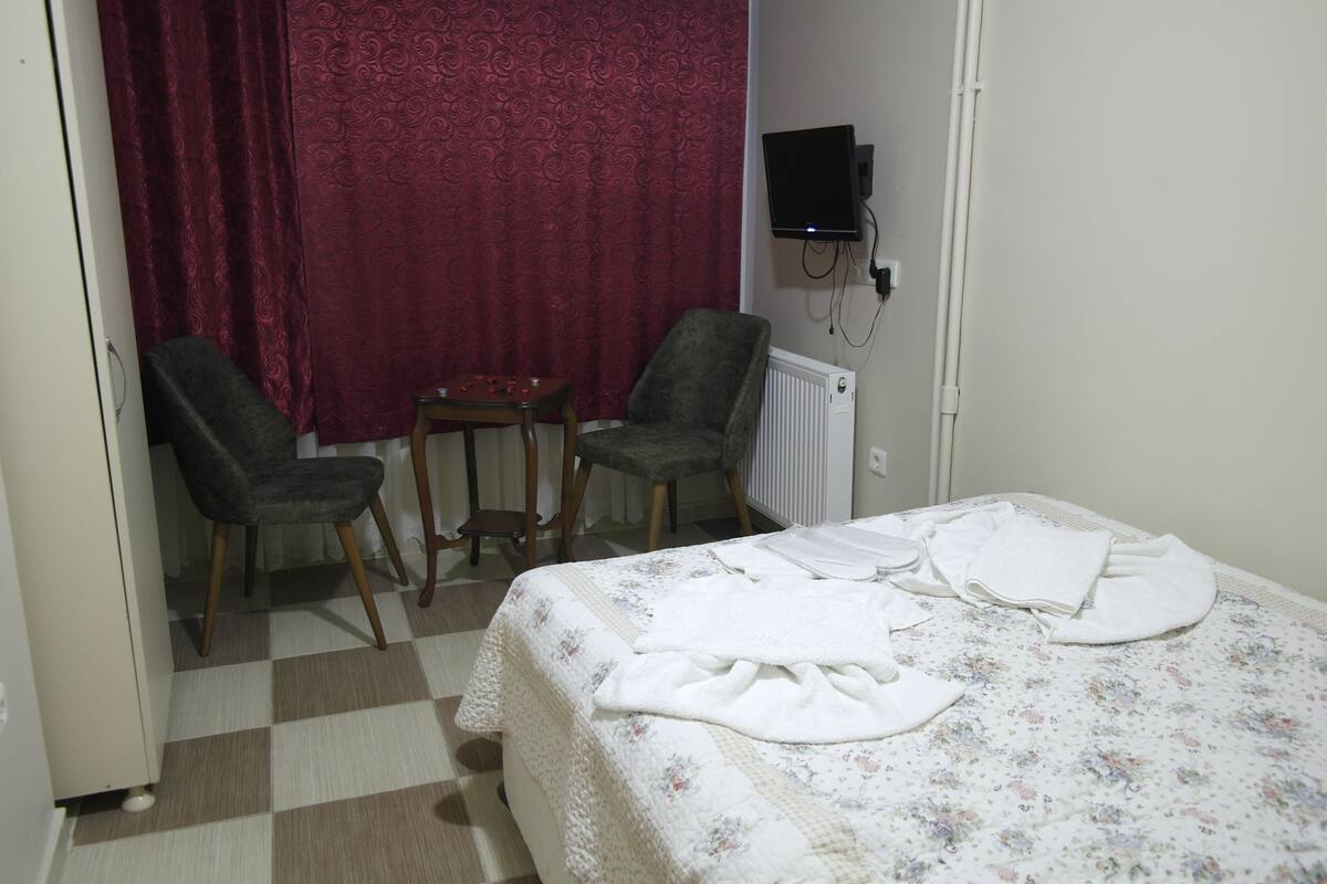 A hotel room with a bed, two chairs, a small table, a TV, and a red curtain.