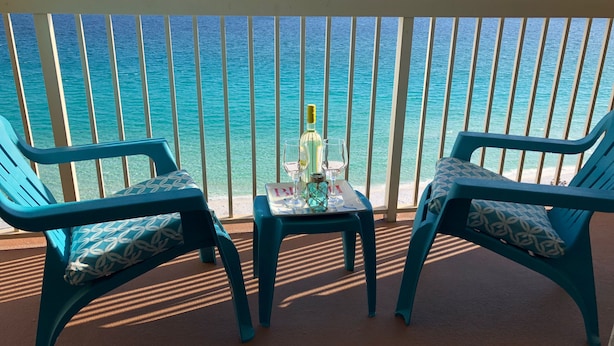 Ein Balkon mit zwei türkisblauen Stühlen und einem kleinen Tisch, auf dem eine Flasche und Gläser stehen.