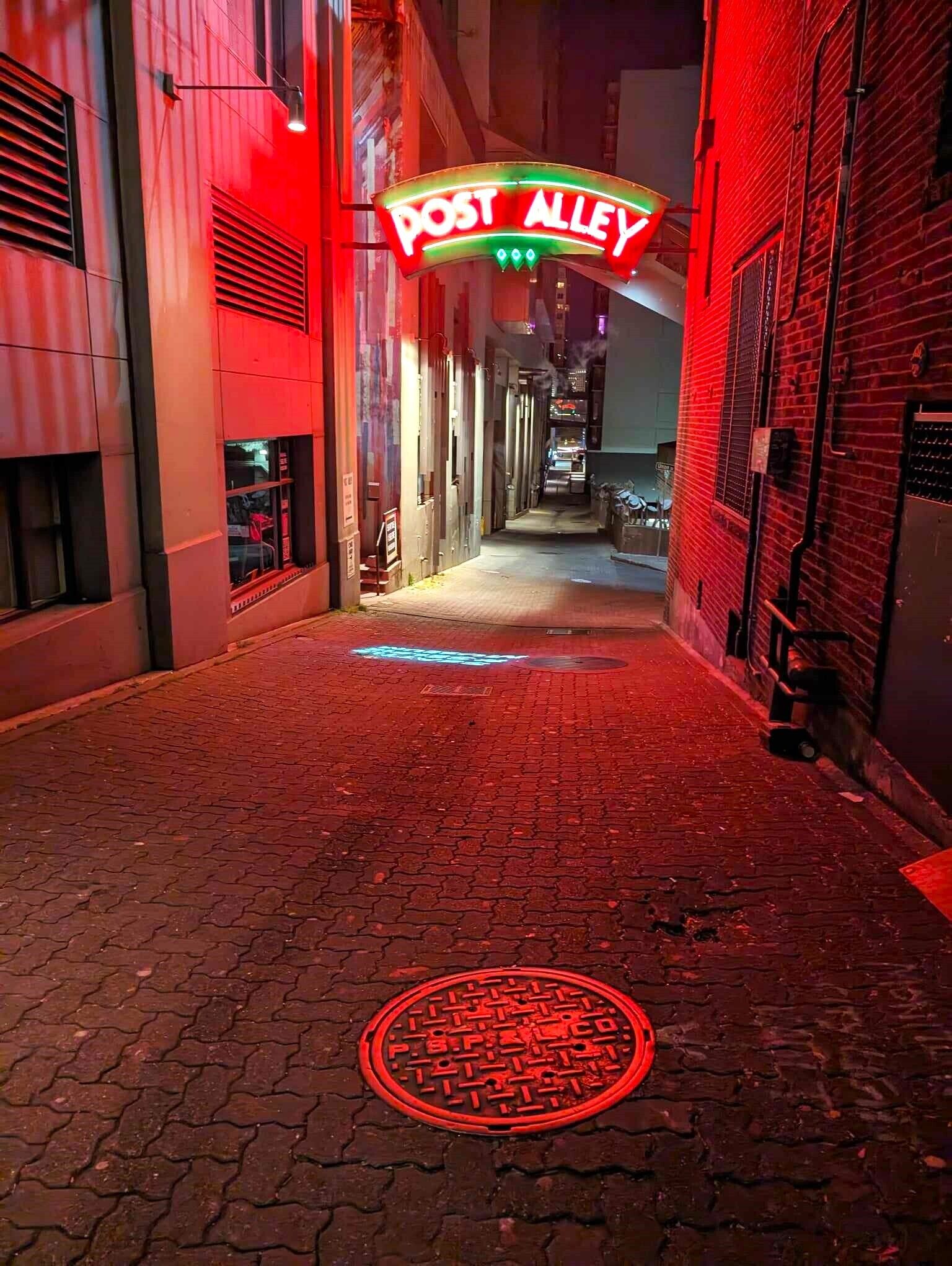 A narrow alleyway with a neon 'POST ALLEY' sign overhead.