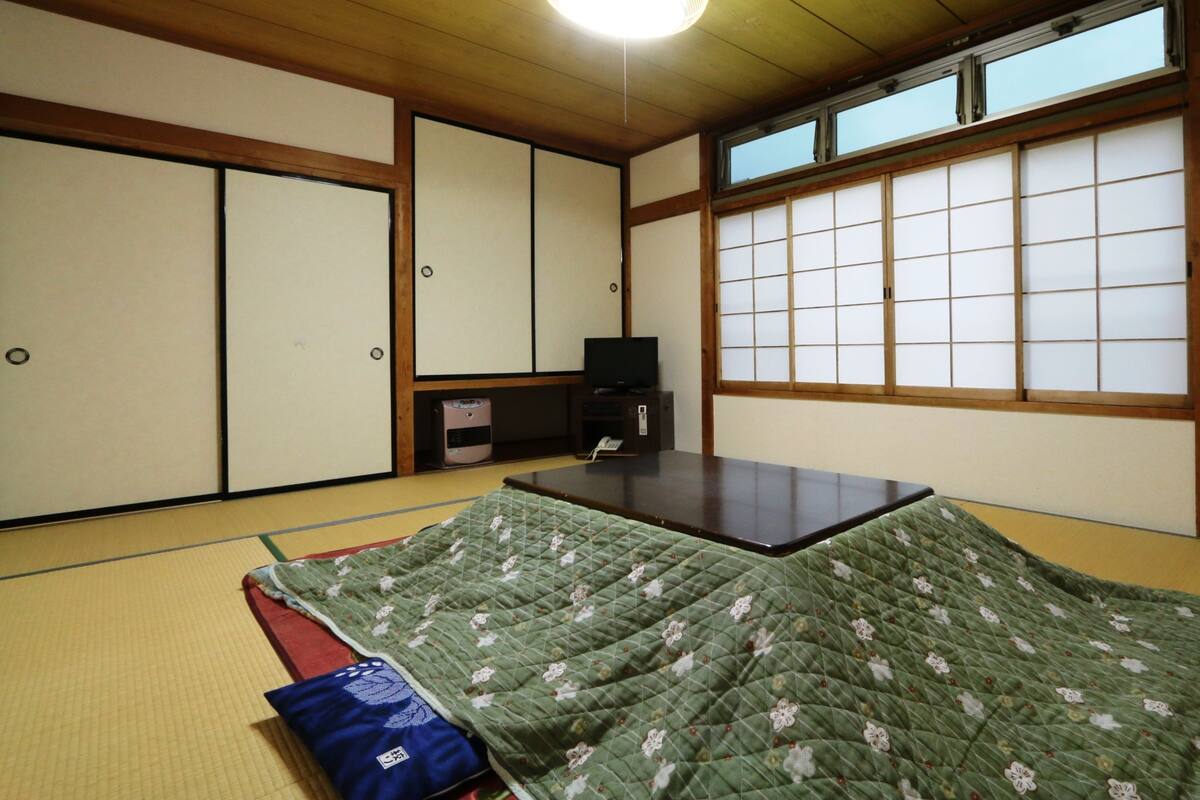 A traditional Japanese room with tatami flooring, sliding doors, a low table, and a bed with a green floral quilt.