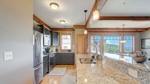 A kitchen with granite countertops, stainless steel appliances, wooden beams, and large windows offering a view. - Chalakee Lodge CH-3- Mountain View, Gated Resort, Indoor/Outdoor Pools & Hot Tub (Boone)