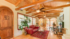A spacious living room with wooden beams, a red leather sofa, a dining table with chairs, and a large window with blinds. - 5,000 sq. ft. Lake villa, 5/5 BA , sleeps 12,  2 boat stalls, 20x40 PRIVATE pool (Hot Springs)